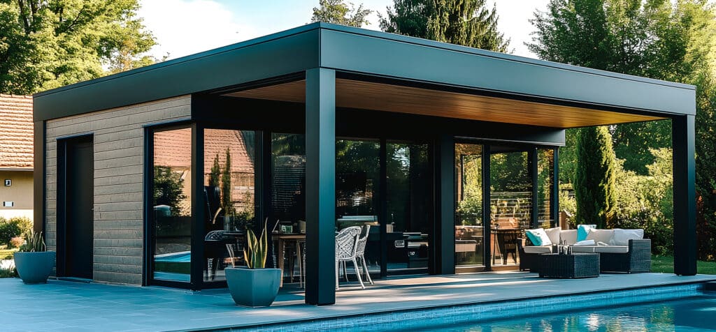 Luxueux pool house moderne noir avec bardage bois foncé et baies vitrées. Espace salon/salle à manger et terrasse au bord de la piscine.