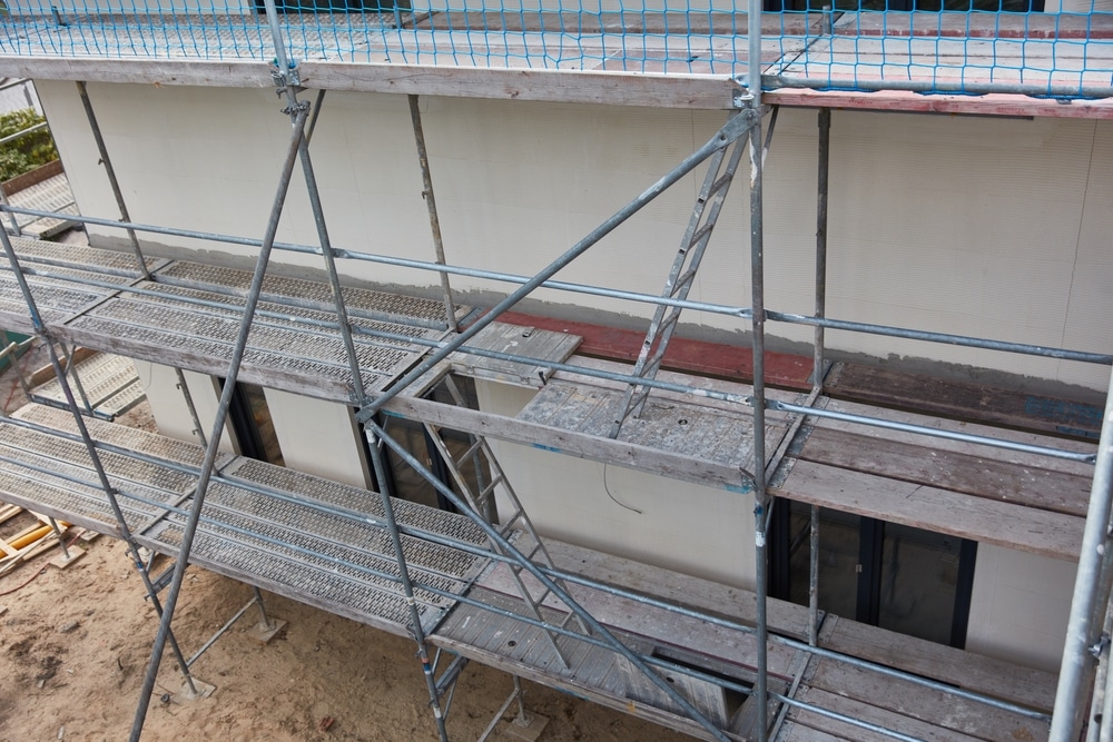 Échafaudage de chantier pour la rénovation de façade Échafaudage professionnel en métal sur la façade beige d'un bâtiment en construction. Vue des plateformes, échelles et filet de sécurité bleu.